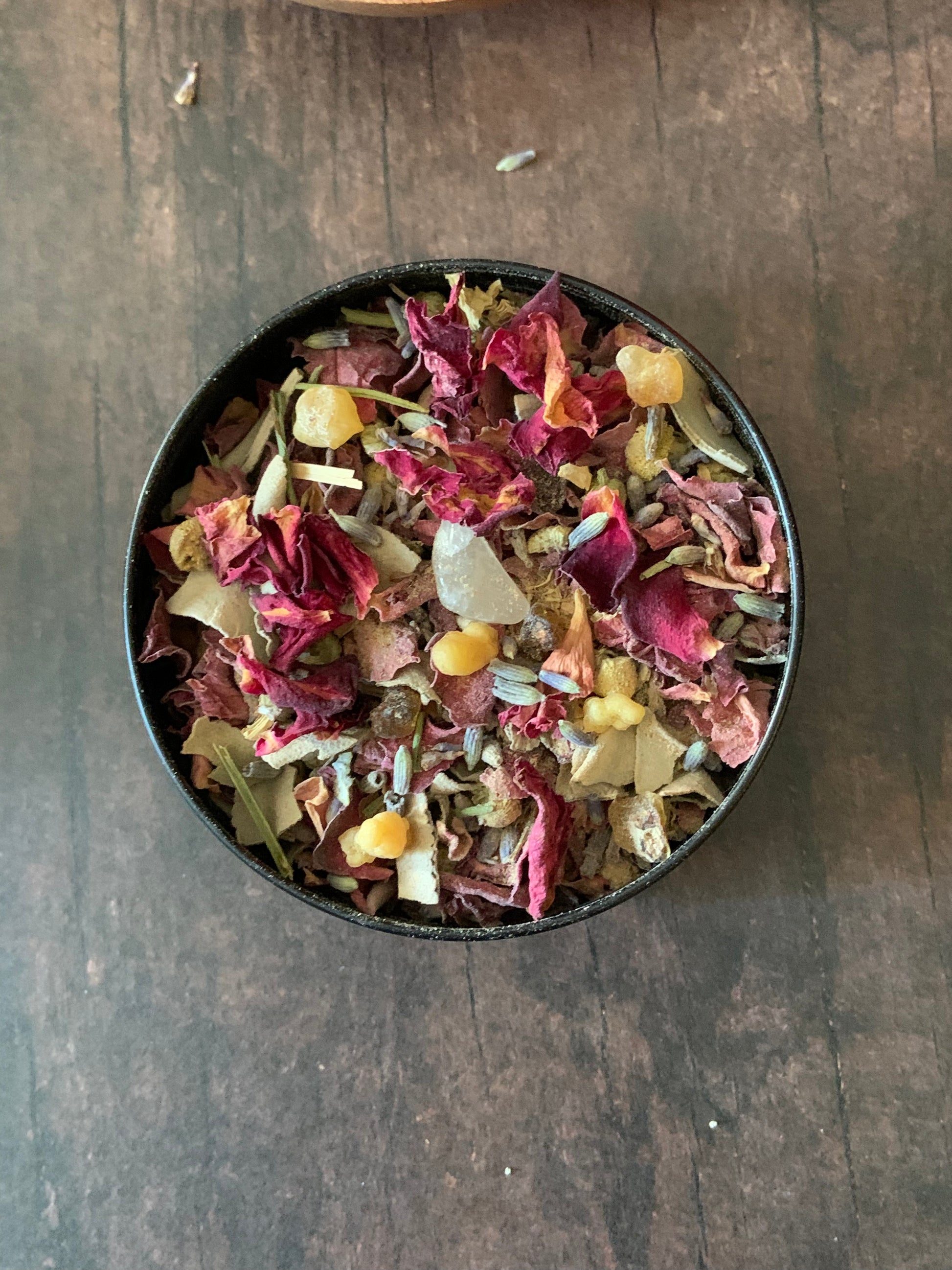 Colorful dried flowers and leaves in a black bowl on a wooden surface