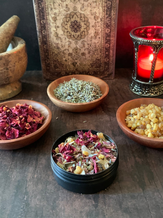 Spices and herbs in bowls on a wooden surface with a lit candle in the background.